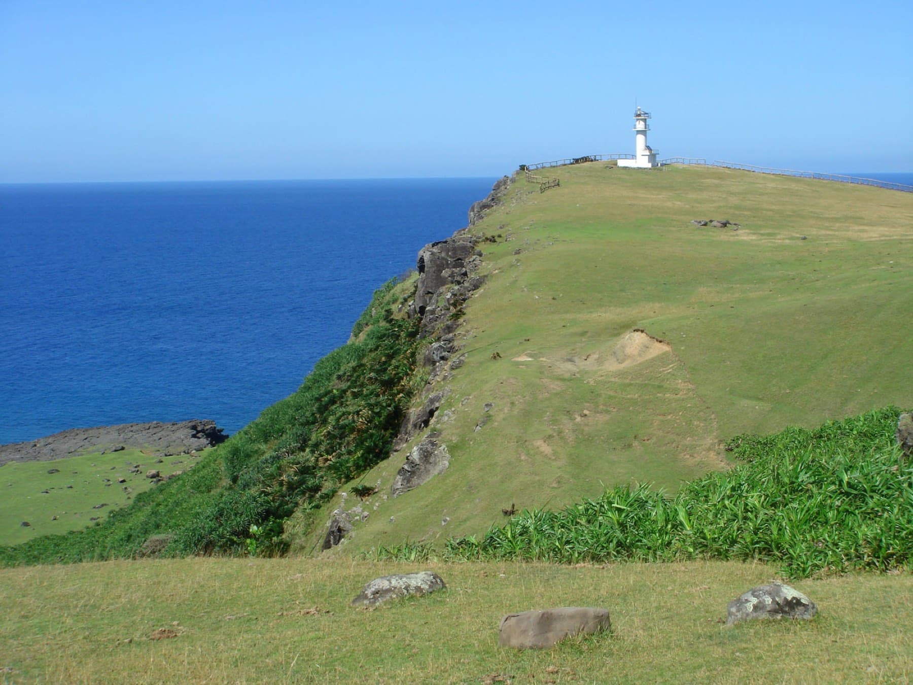 The long green ridge of Agarizaki runs out to a small white lighthouse above steep cliffs and deep blue sea at the eastern tip of Yonaguni.