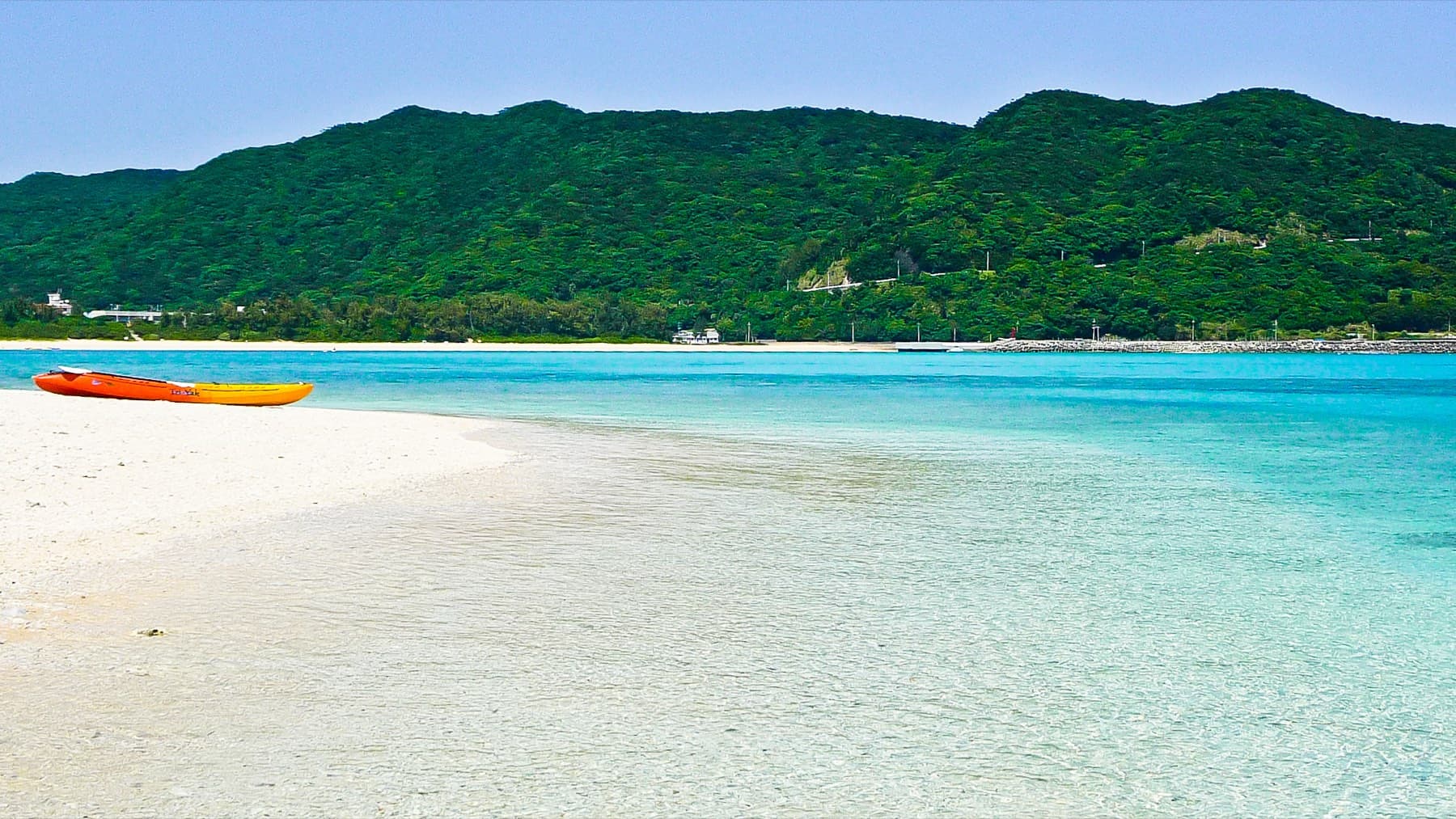 Two kayaks rest on a spit of white sand at Aharen Beach on Tokashiki, where shallow clear water meets the green hills behind the village