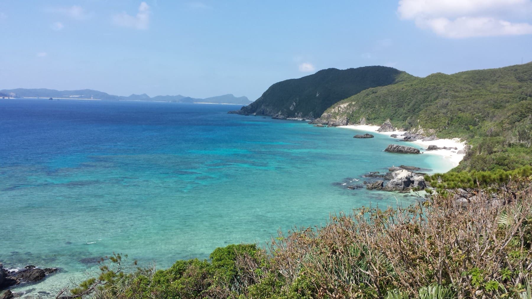 From the Aharen observation deck the coast of Tokashiki runs north in a line of green headlands and small white coves above blue water