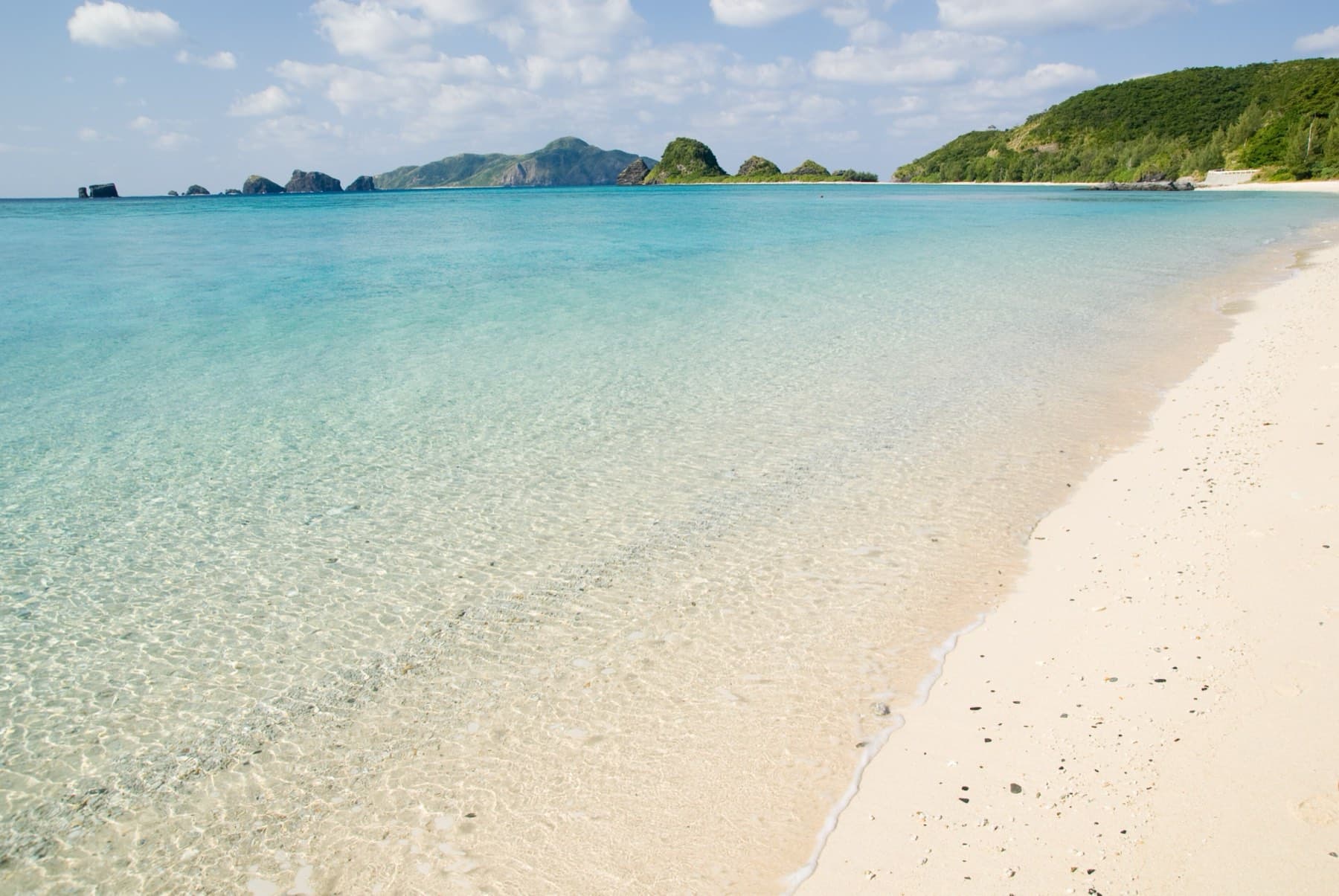 Clear shallow water laps the white sand of Ama Beach on Zamami as the rocky outlines of small uninhabited islets line the horizon to the south