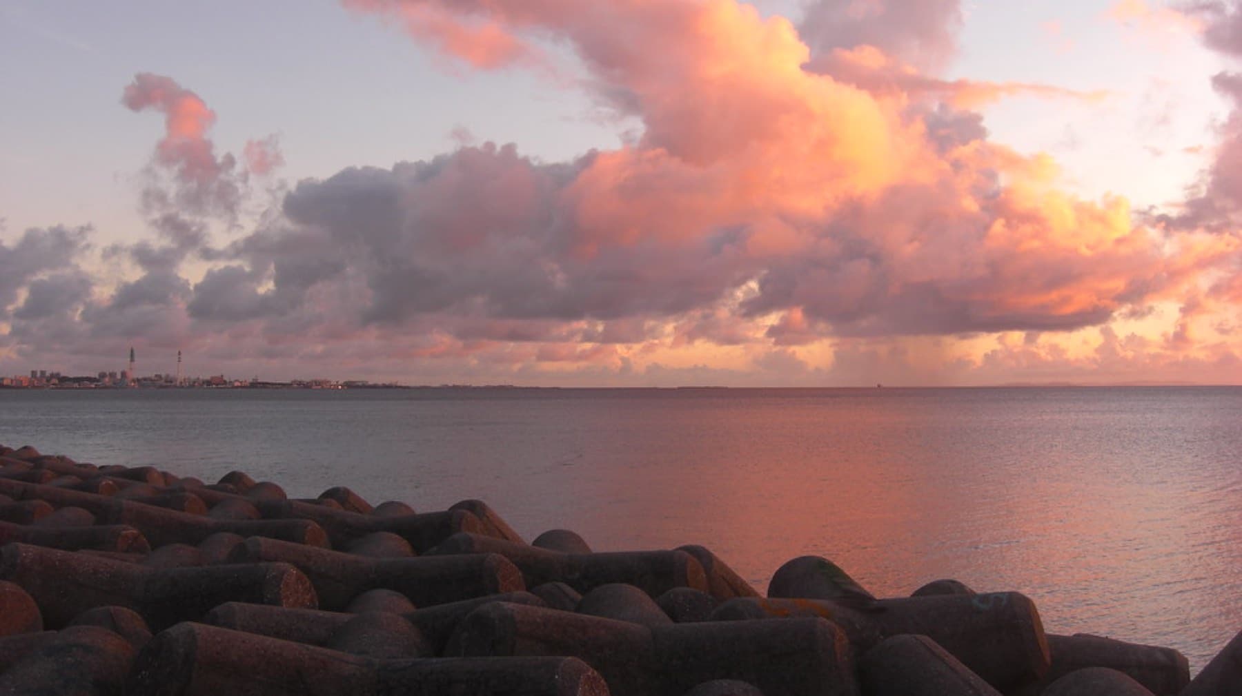 Pink and orange clouds glow over the calm East China Sea at sunset, seen from the tetrapods of the Mihama seawall in Chatan