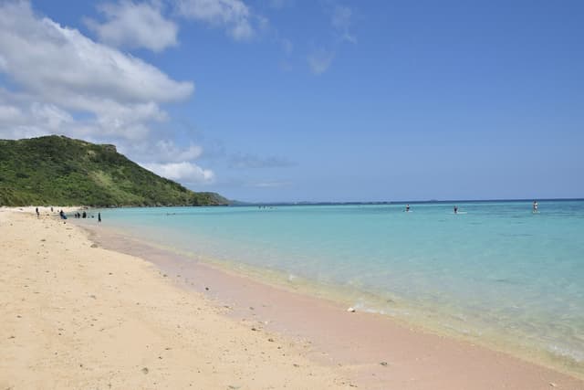 Clear shallows over the reef lap a long strip of pale sand at Aragusuku Beach as a green headland closes the far end of the bay.