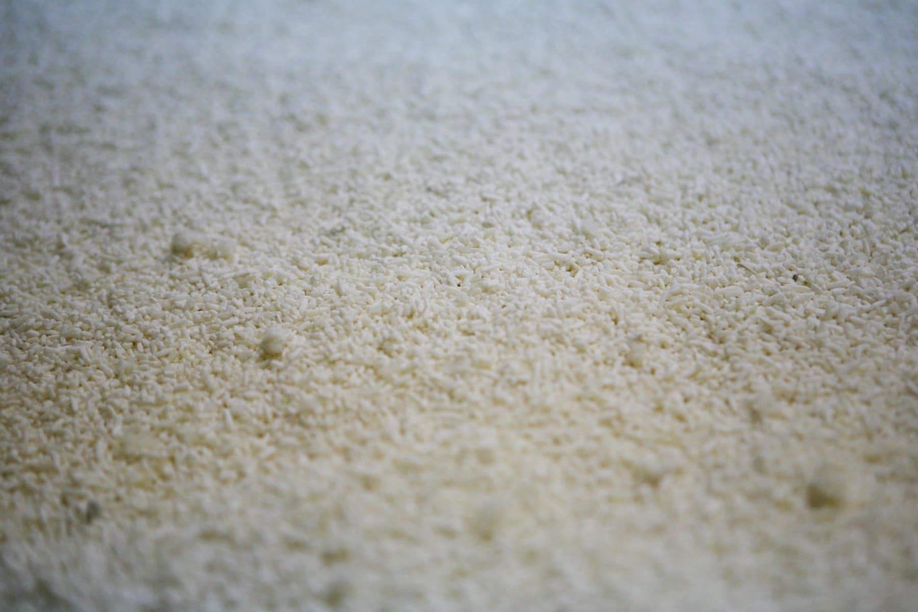 A distillery worker turns a long bed of steamed rice and koji with a wooden paddle inside a steel-walled fermentation room on Ishigaki