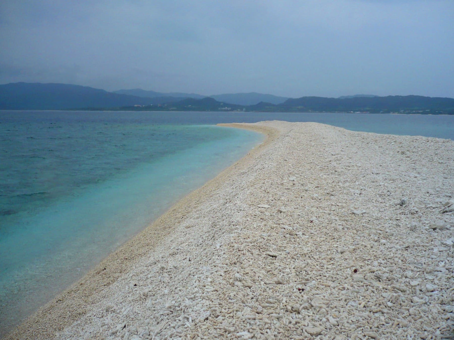 A bare spit of broken white coral runs out into milky turquoise water at Barasu, with the hills of Iriomote low on the horizon.