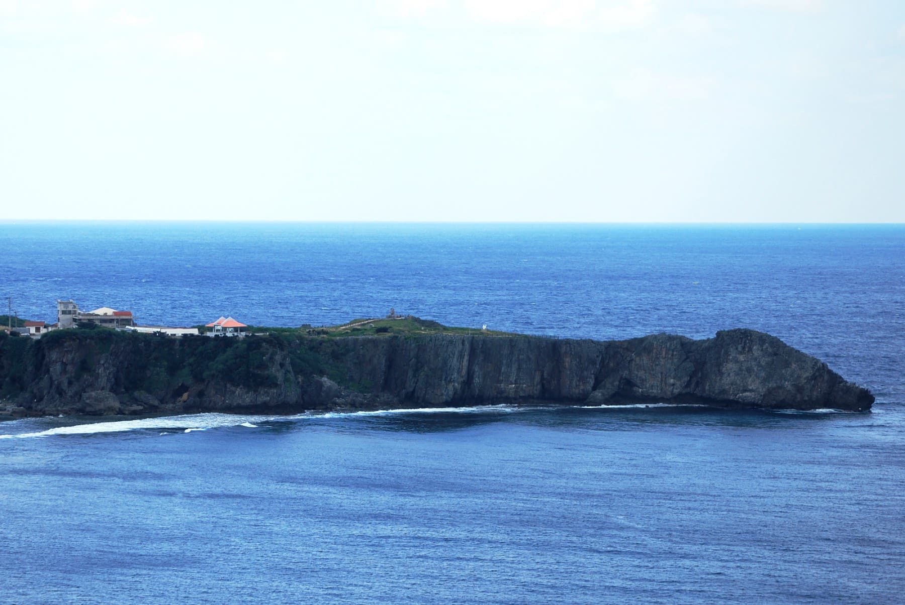 The flat-topped headland of Cape Hedo runs out into deep blue sea at the northern tip of Okinawa Island, edged by dark cliffs and white surf