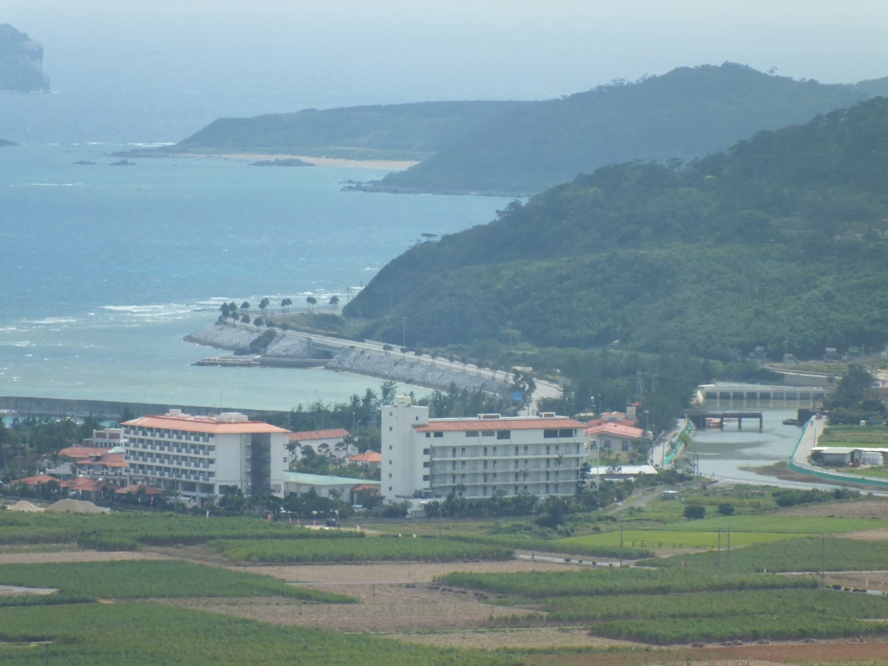 From the hill at Tounnaha the resort hotels of the Eef Beach area sit among cane fields on Kume-jima, and a breakwater curves out below a forested headland
