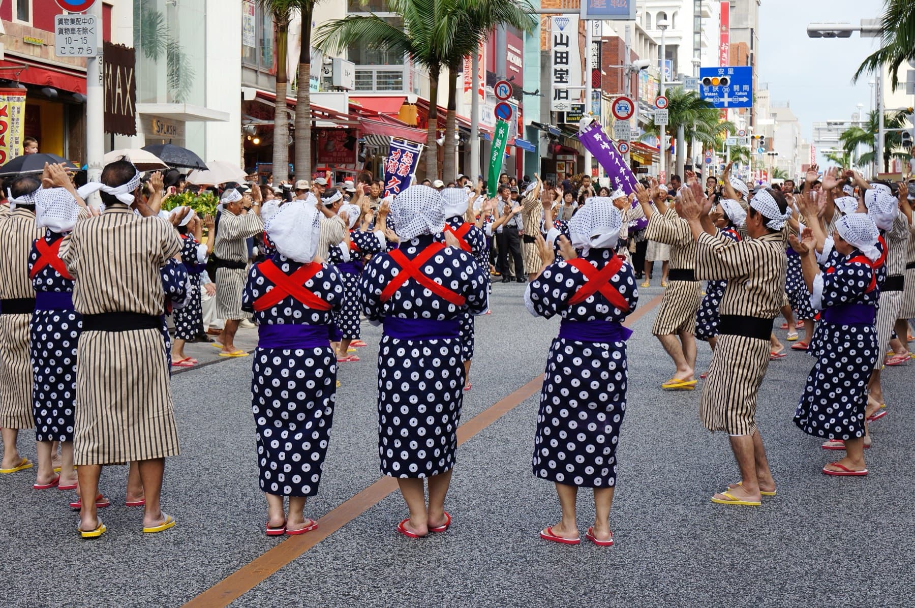 Rows of hand dancers in white head cloths, polka-dot kimono and red sashes raise their arms in step along Kokusai-dori during the Shuri Castle Festival parade
