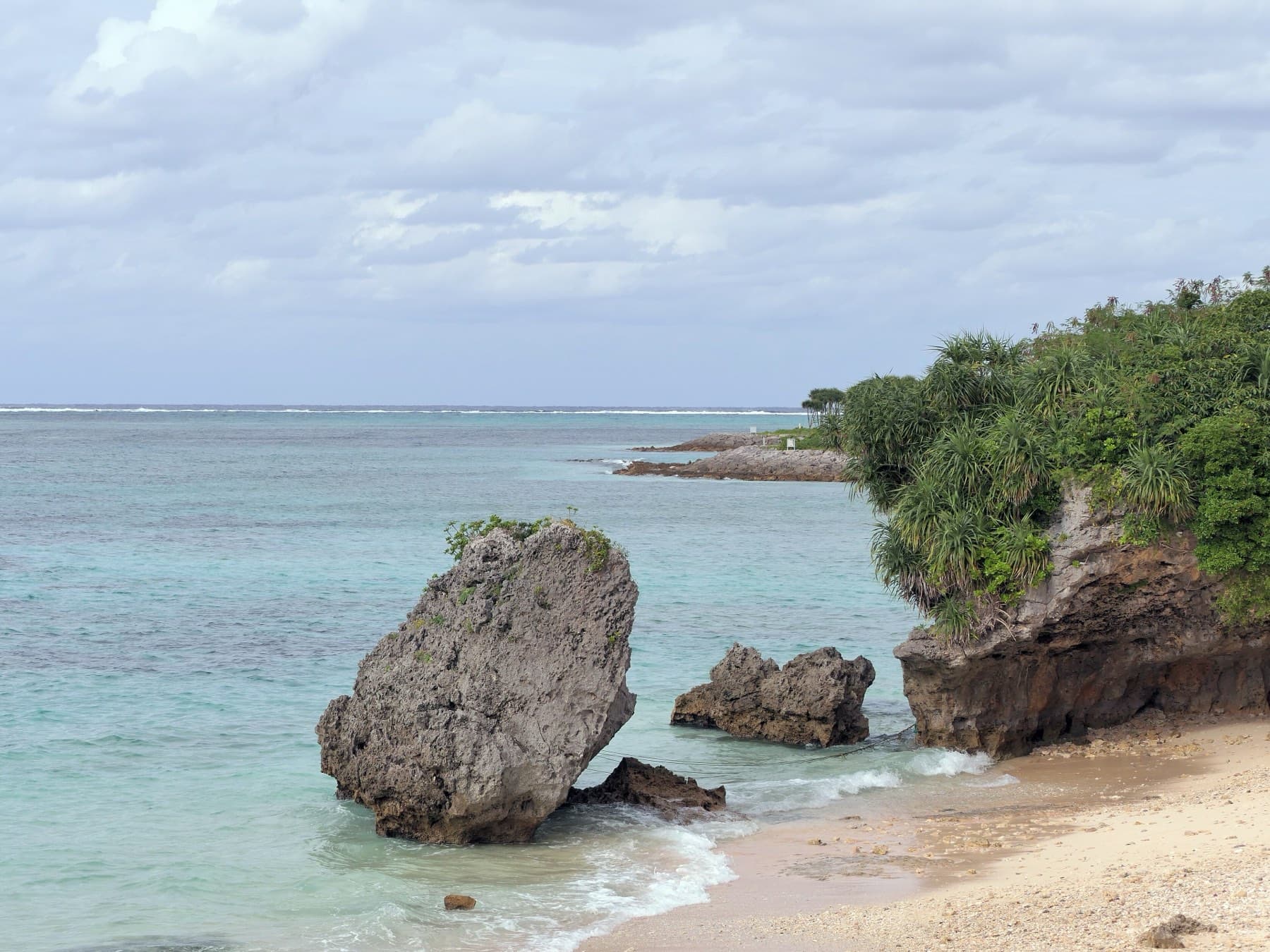 A tall limestone boulder stands in the clear shallows at Emerald Beach in Ocean Expo Park, and small waves curl around its base onto the sand