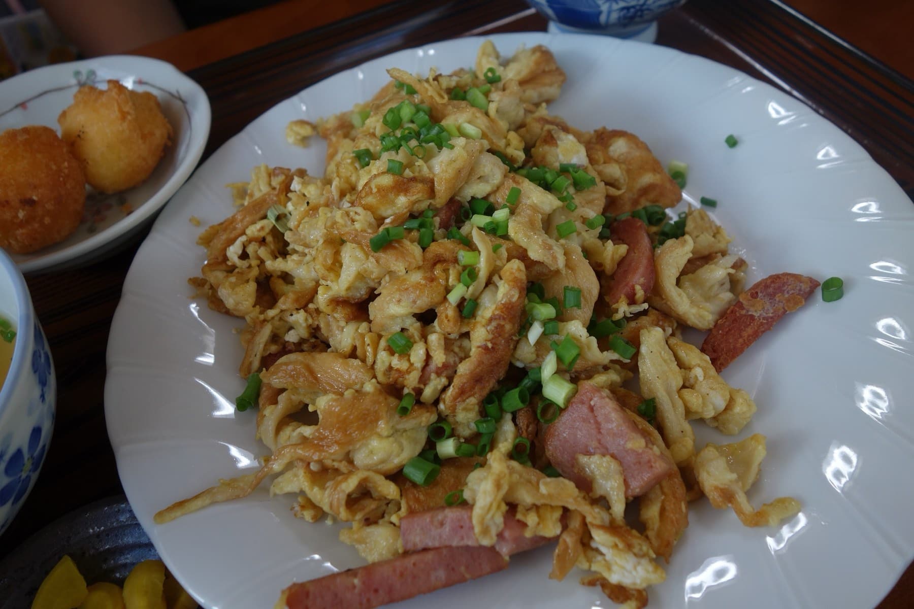 Egg-soaked wheat gluten stir-fried with luncheon meat and green onion fills a white plate at Shirasa on Kouri, with sata andagi in a dish behind