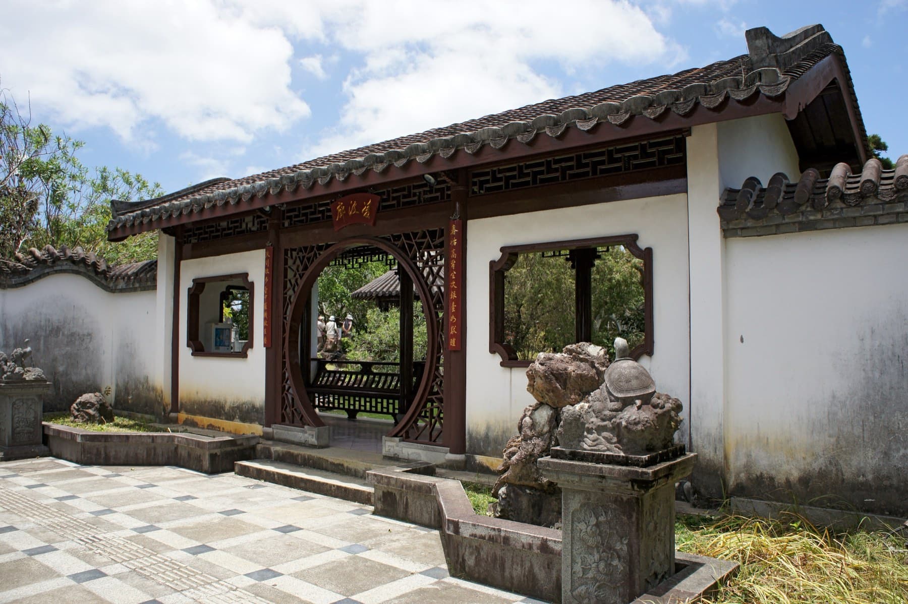A round doorway in a white garden wall at Fukushuen opens onto a pavilion, and a stone turtle sits on a carved rock beside the entrance