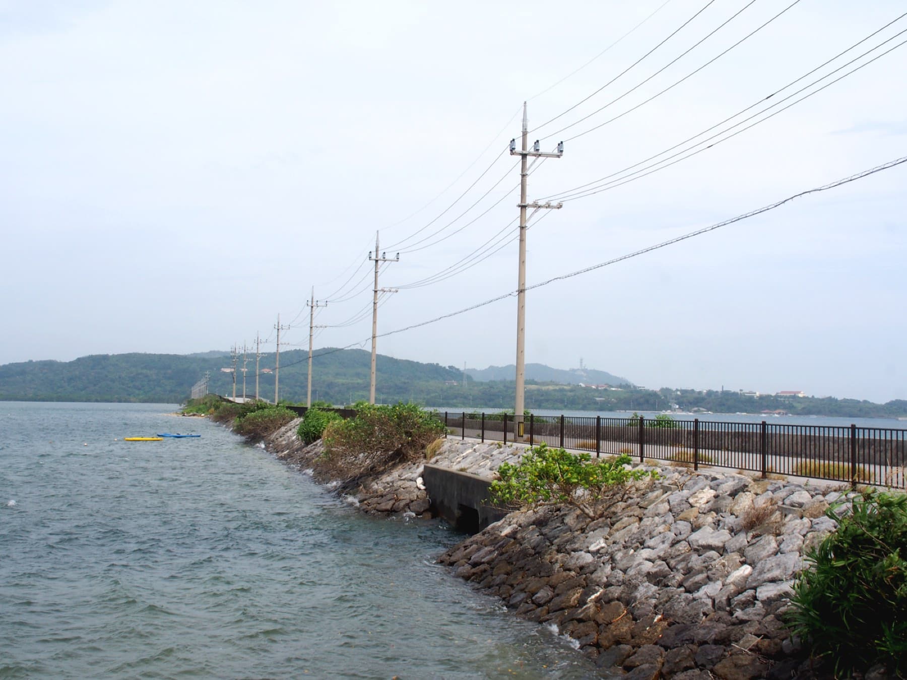 The Funaura Causeway carries the road and a line of power poles low across the water of Funaura Bay toward the hills of Iriomote.