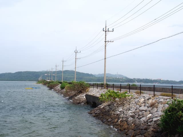 The Funaura Causeway carries the road and a line of power poles low across the water of Funaura Bay toward the hills of Iriomote.