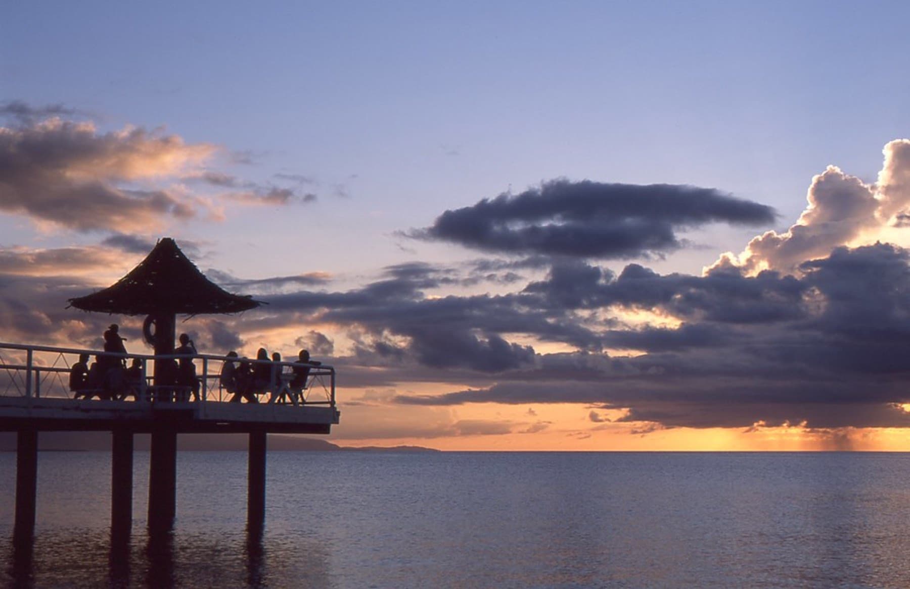 After sunset a lavender sky hangs over the still water at Fusaki Beach as people gather in the thatched gazebo on the pier.