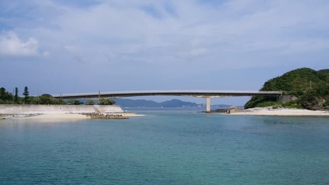 The low Geruma Bridge crosses a calm green channel from Geruma toward a wooded islet, and white sand edges the shore on both sides