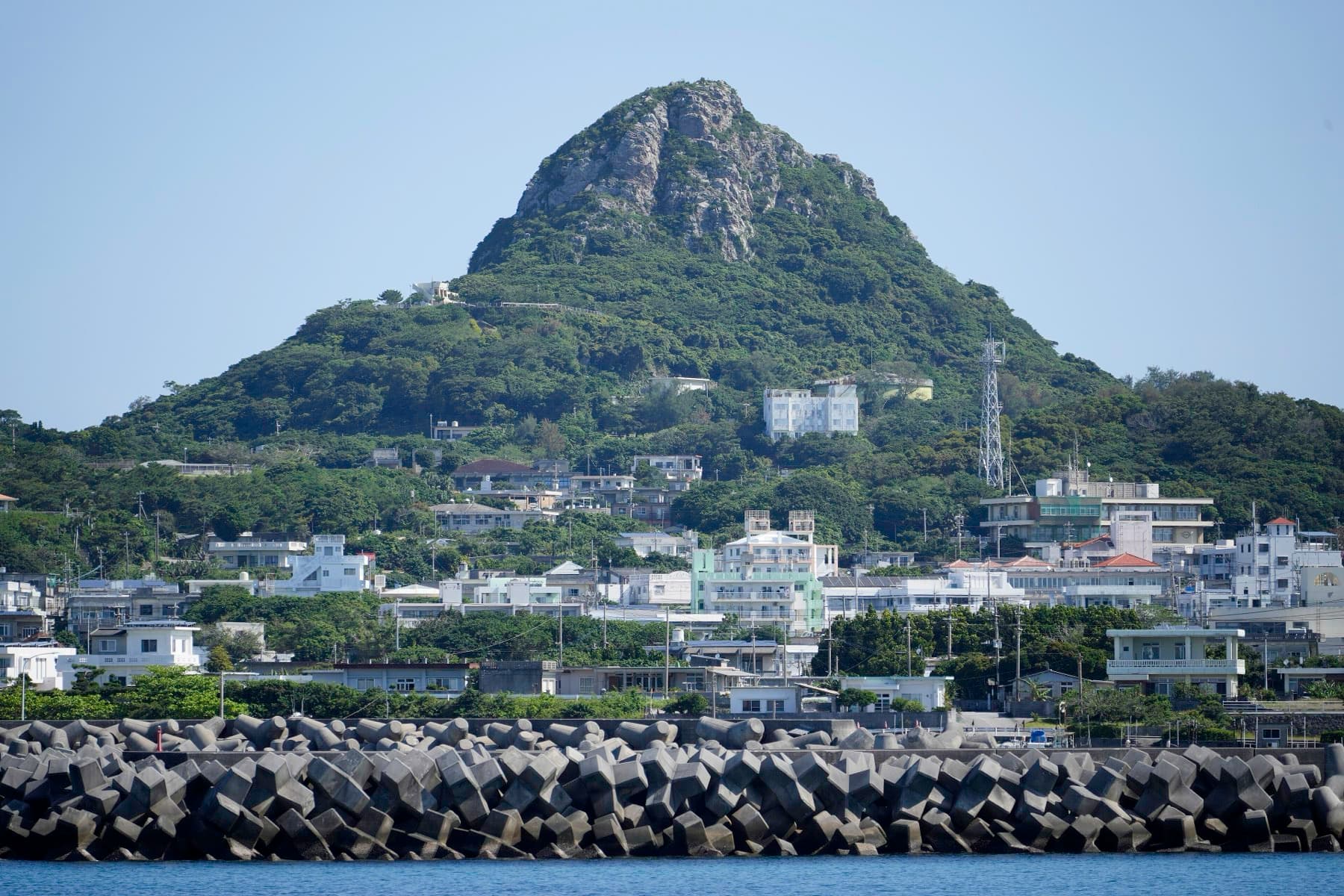 The rocky cone of Gusuku-yama rises above the white houses of Ie village as the ferry from Motobu approaches the harbour wall