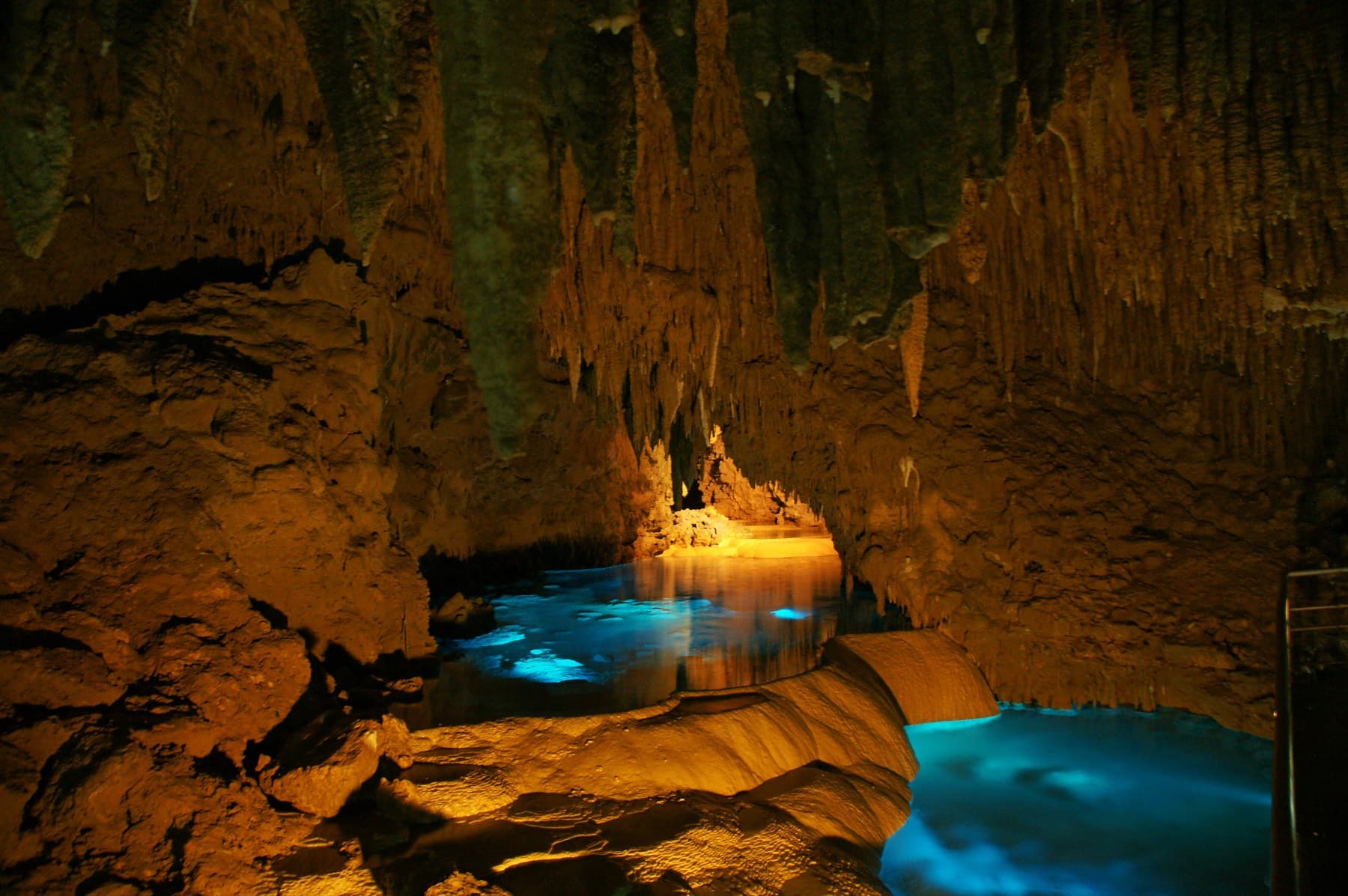 Rimstone terraces step down into a pool of glowing blue water under dripping formations in the Gyokusendo cave