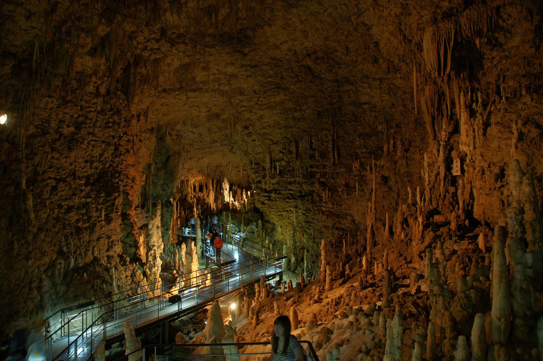 Thousands of stalactites hang from the ceiling of the Gyokusendo cave above a lit walkway that winds into the warm-lit chamber