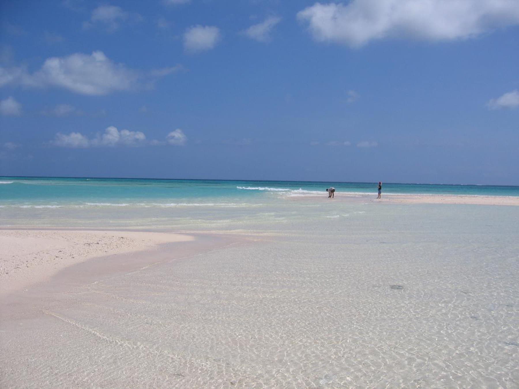 Rippled pale sand runs into clear shallow water on Hatenohama, and two distant figures stand on the far end of the bar under a blue sky
