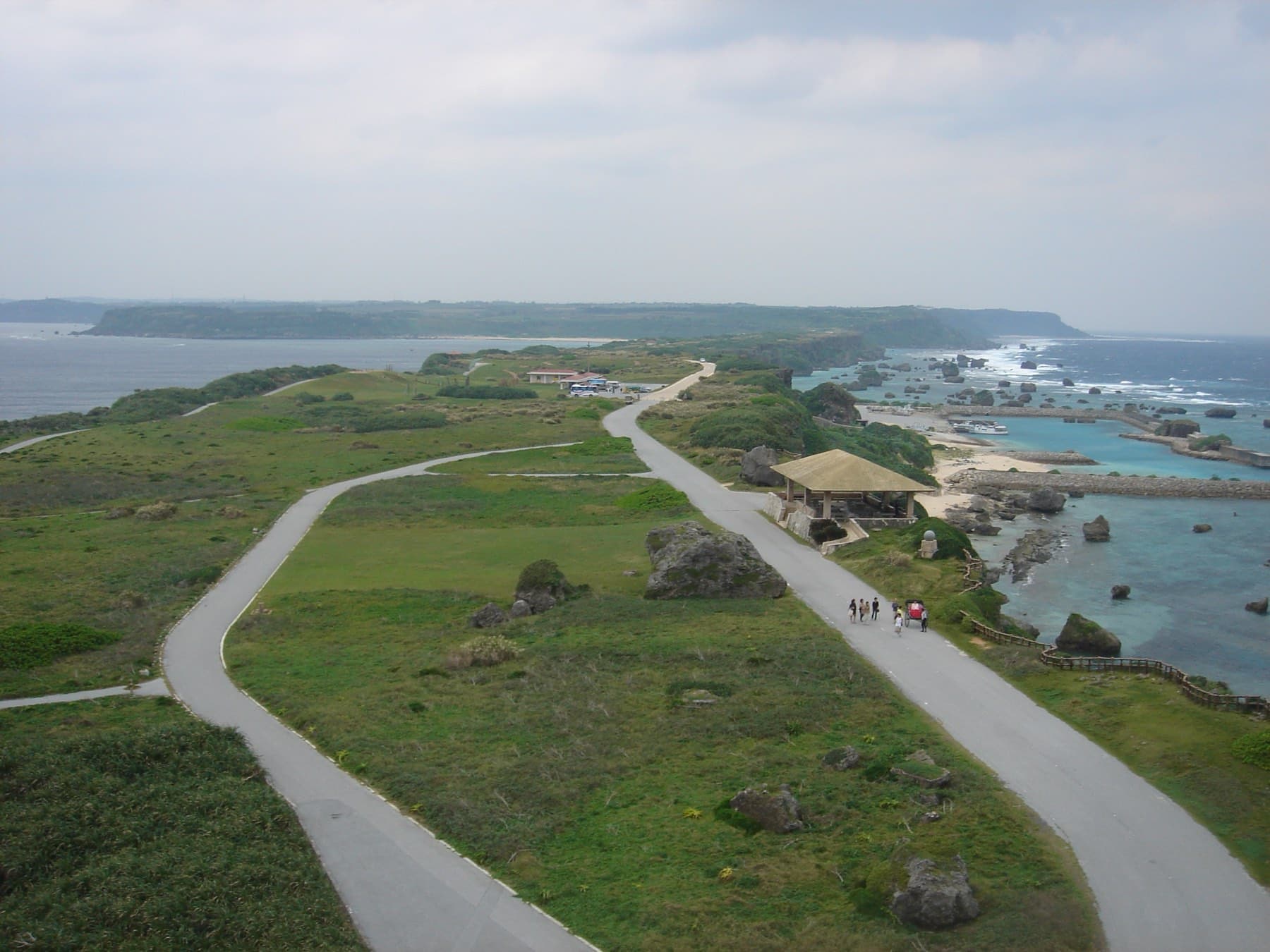 The view from the lighthouse follows the road as it loops over the long grassy cape of Higashi-Hennazaki above a coast scattered with coral boulders.