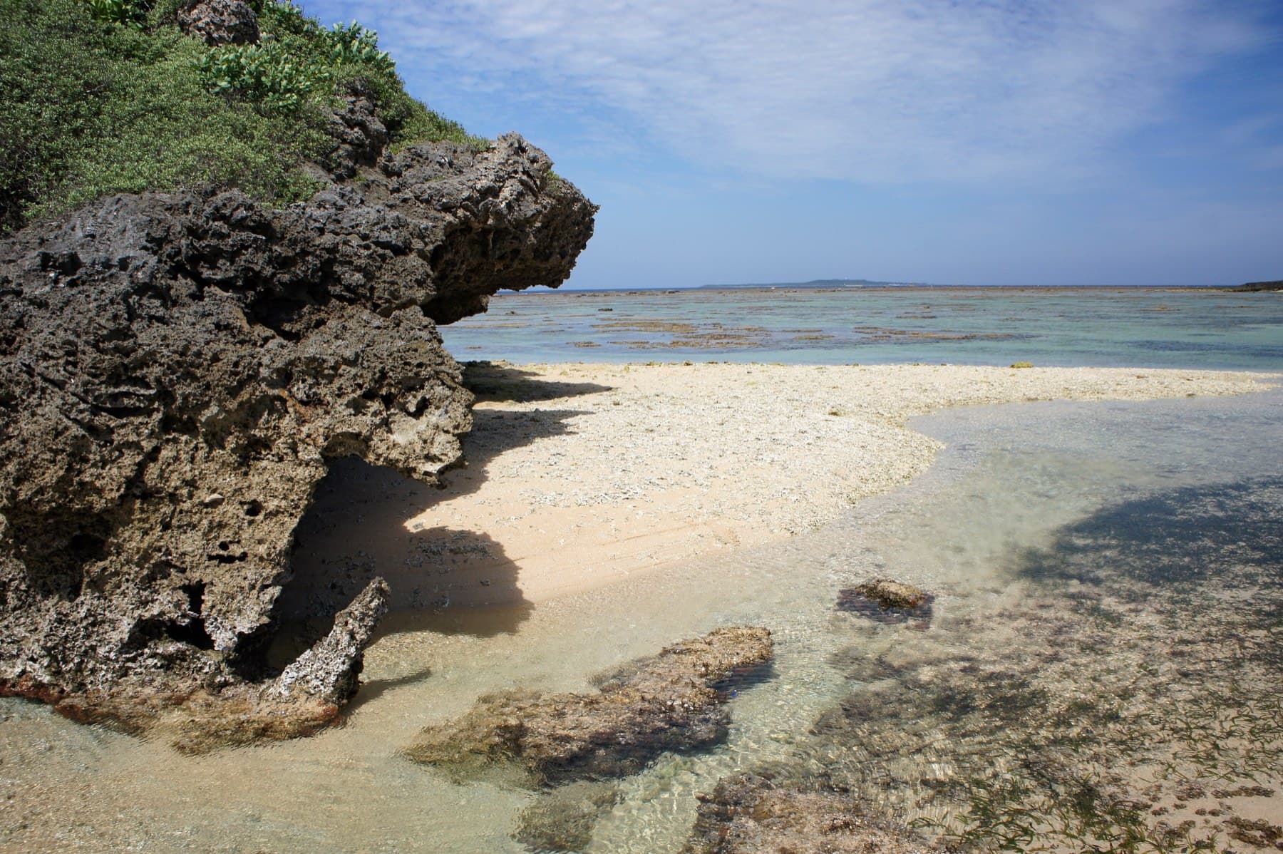 An undercut limestone outcrop shades a corner of the coral sand at Hoshizuna Beach as the reef flat runs out to the sea.