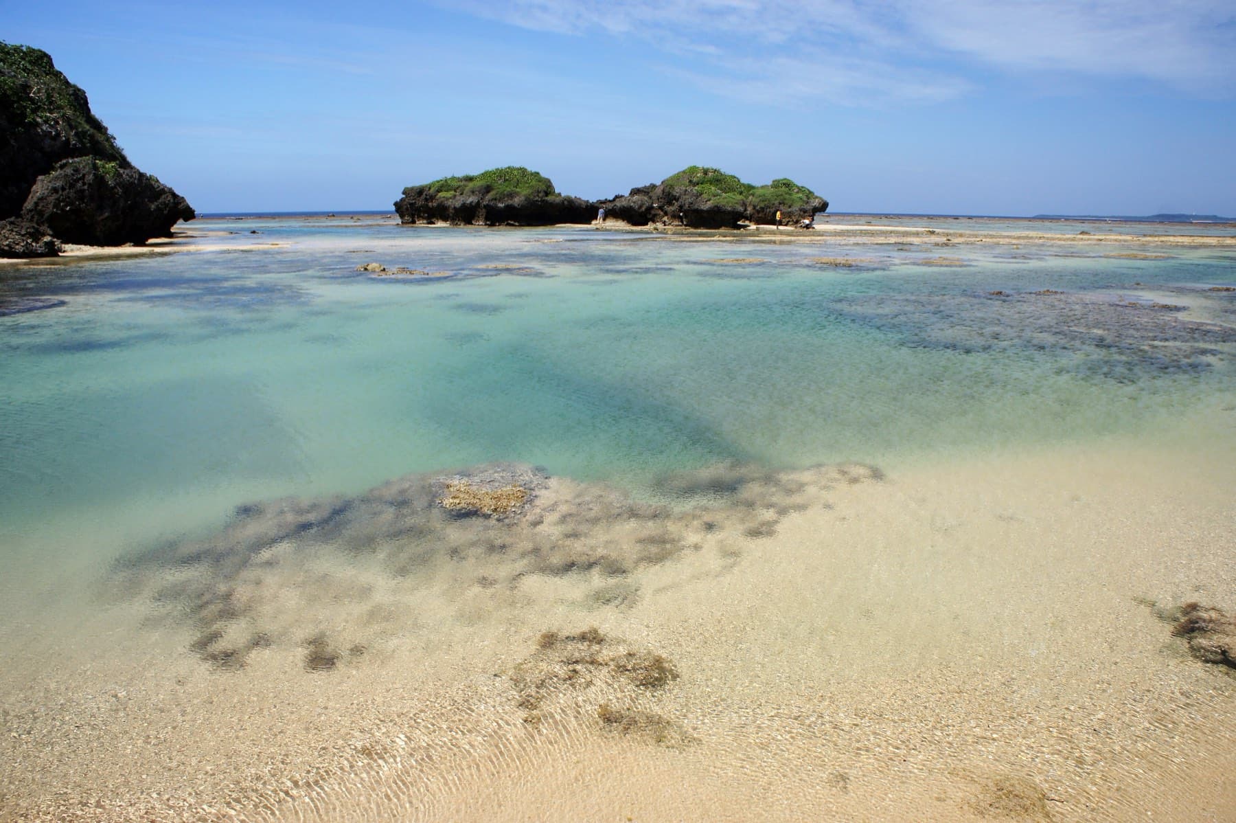 Turquoise tide pools fill the reef flat at Hoshizuna Beach, and two rocky islets sit just offshore under puffy cloud.
