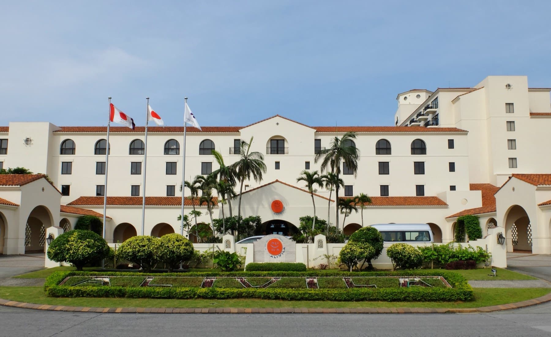 Palms and clipped hedges line the circular drive in front of the cream Spanish-style facade of Hotel Nikko Alivila under a blue sky