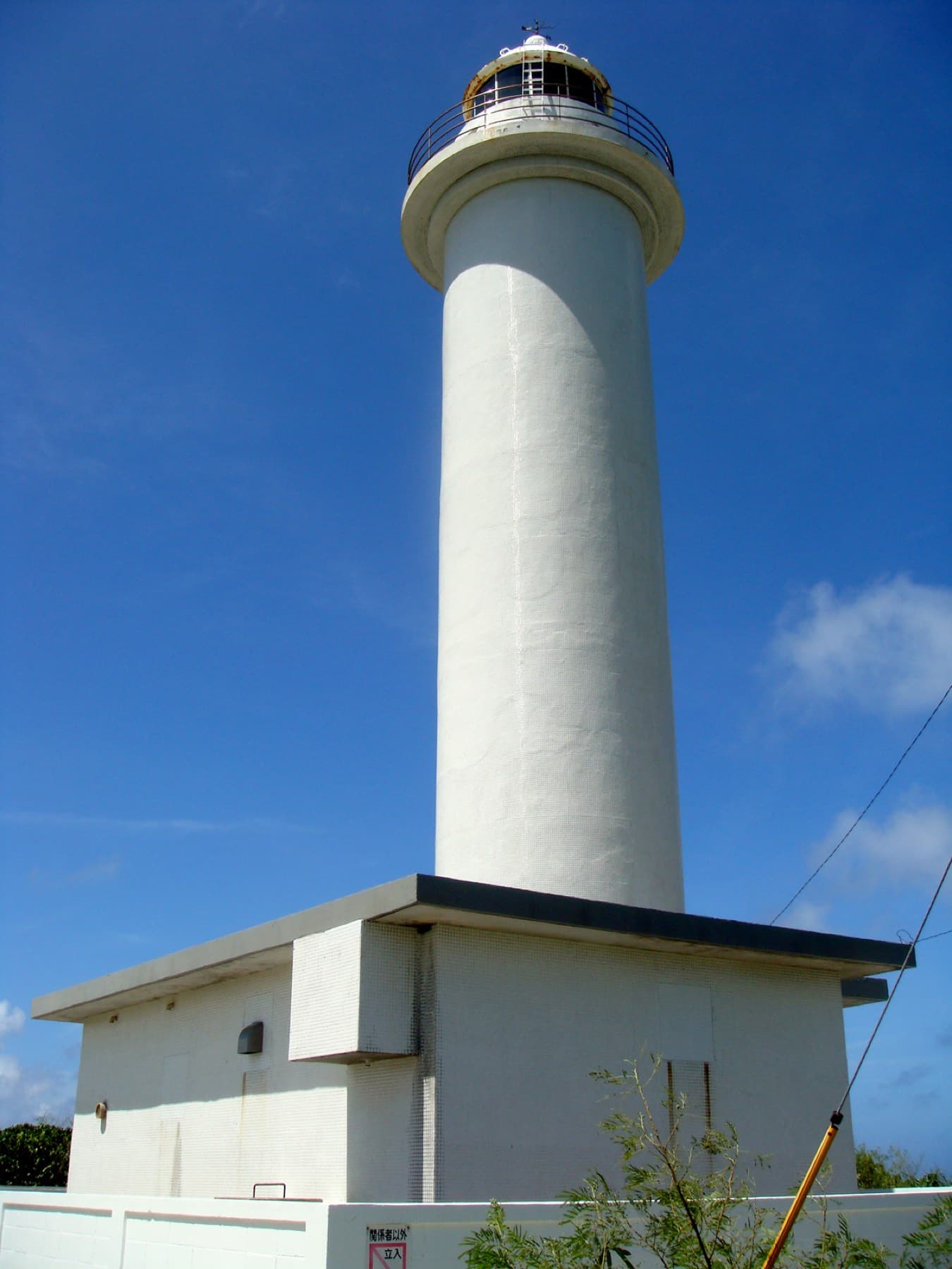 The white Ikema lighthouse stands above its small square base against a deep blue sky on the north side of the island.