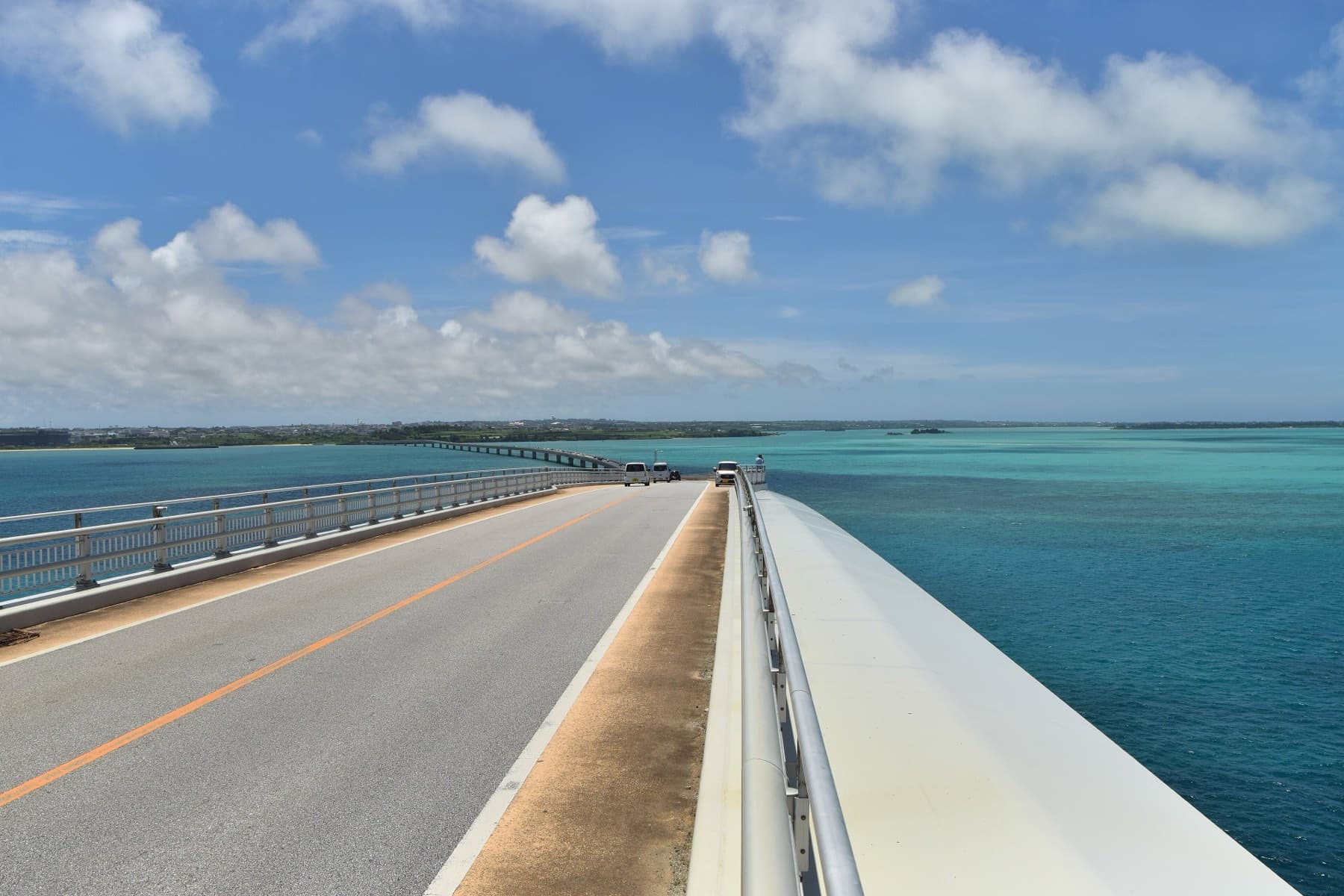 The two-lane deck of the Irabu Bridge runs ahead between low railings with open sea on both sides and Irabu on the horizon.