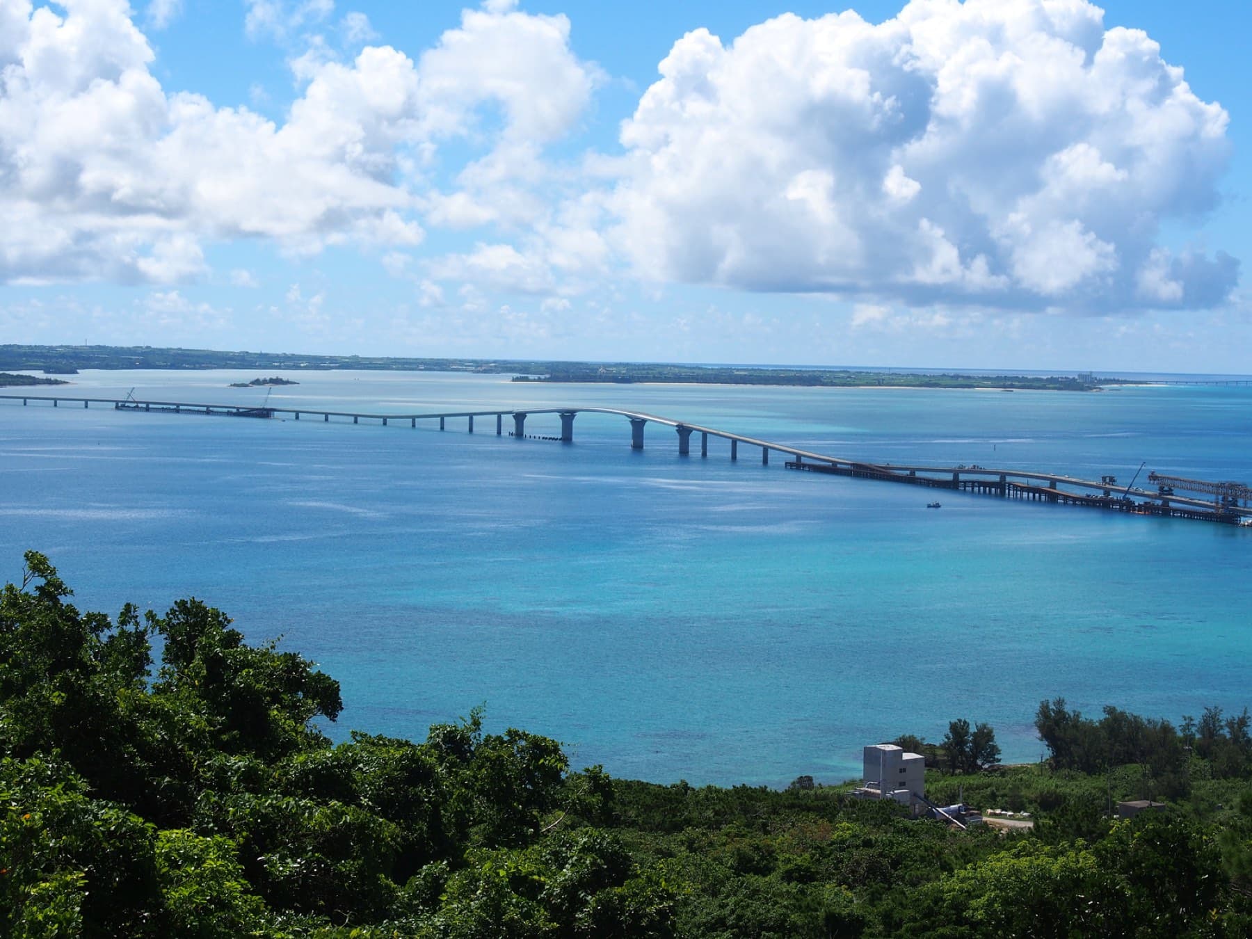 From the Makiyama lookout on Irabu the long curve of the Irabu Bridge crosses deep blue water toward Miyako under a pile of summer cloud.