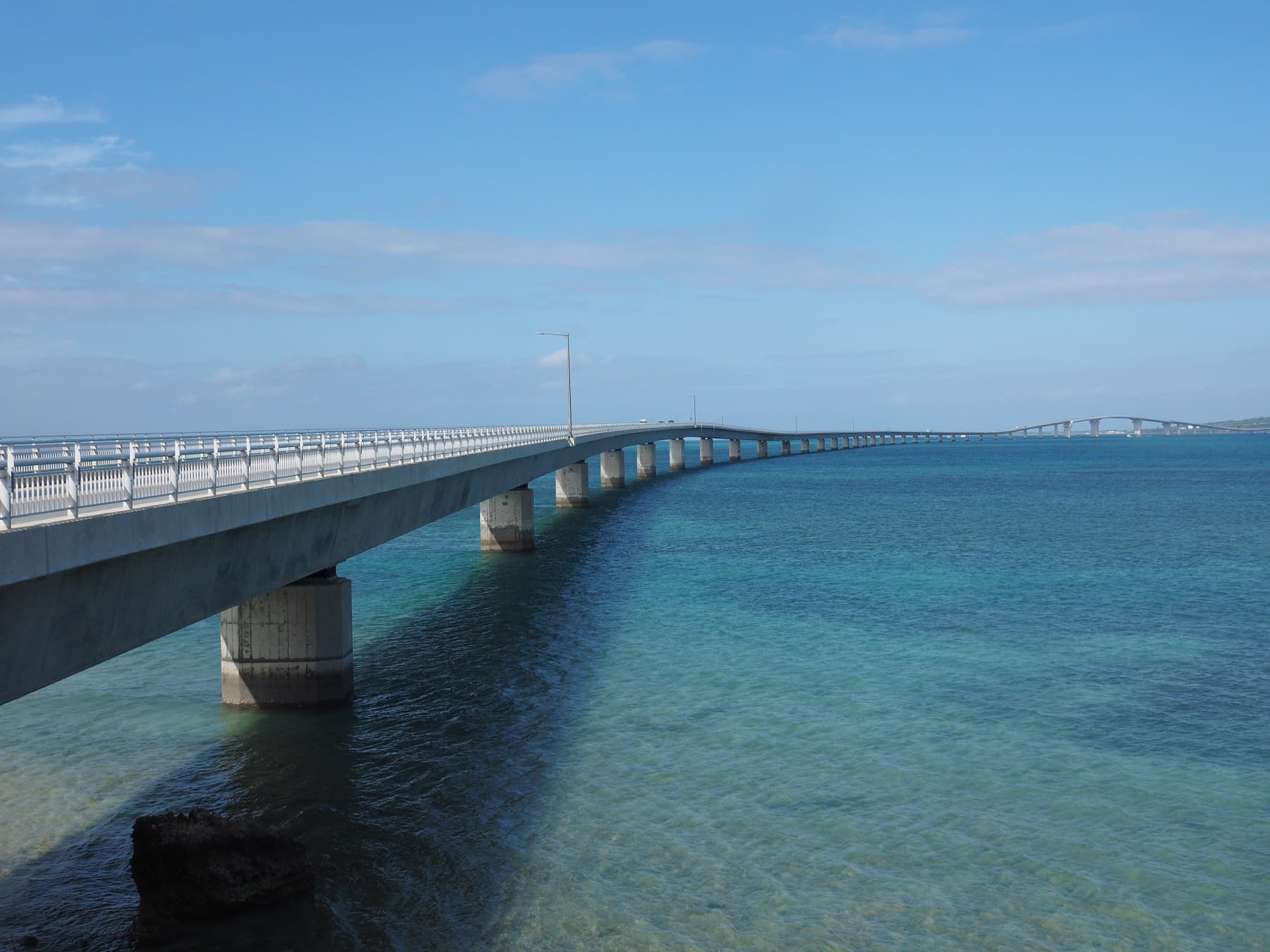 Concrete piers carry the low span of the Irabu Bridge across clear turquoise shallows as it heads out toward its high arch over the channel.