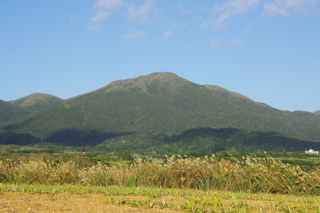 Mount Omoto rises green and forested above pale grassland in the middle of Ishigaki on a clear winter day.