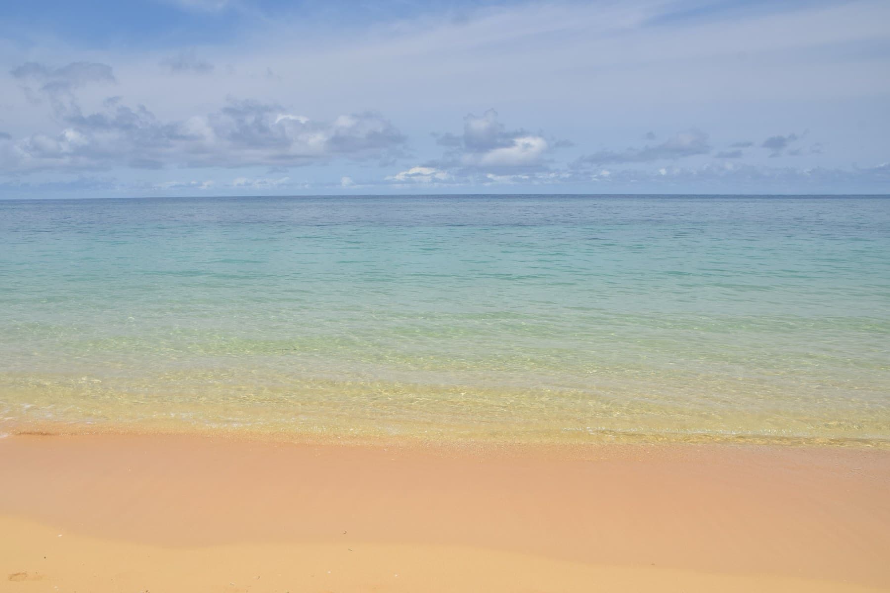 Pale sand slopes into calm water that turns from green to deep blue toward the reef line off Ishigaki Sunset Beach.