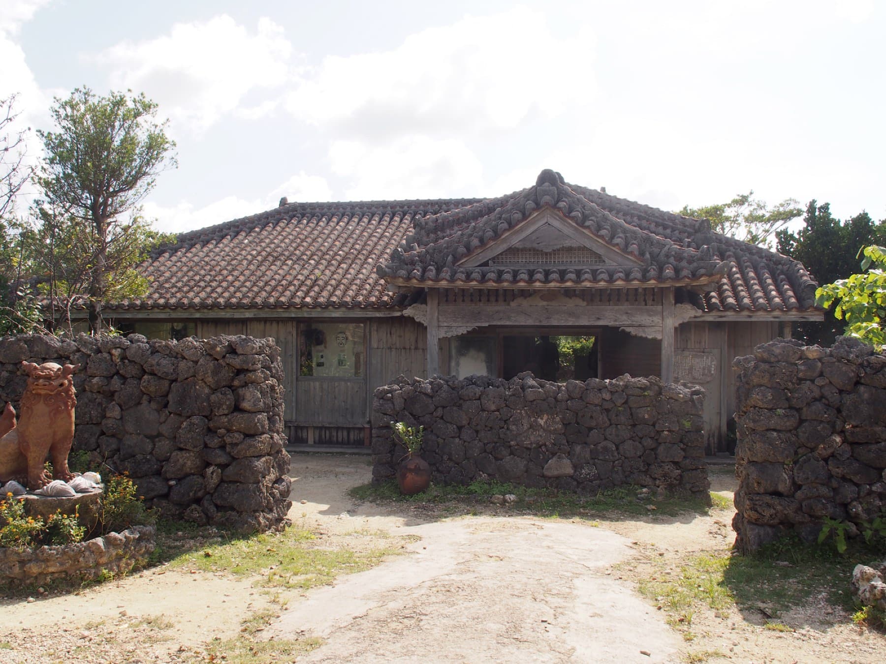 Coral-stone walls and a clay shisa guard the gate of the old red-tiled Makishi house at Ishigaki Yaima-mura.