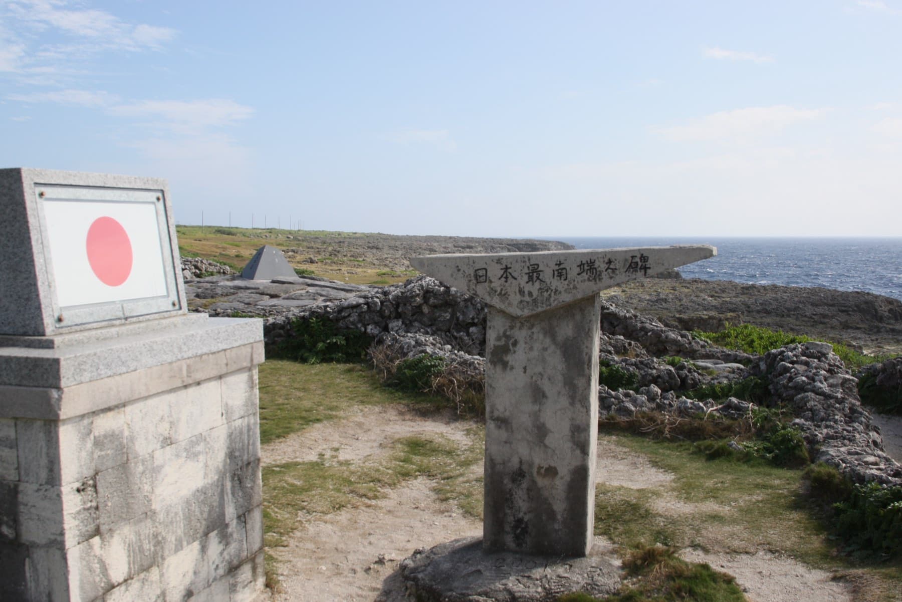 Stone markers and a pillar painted with the Japanese flag stand among the coral rock and grass at Japan's Southernmost Monument on Hateruma.