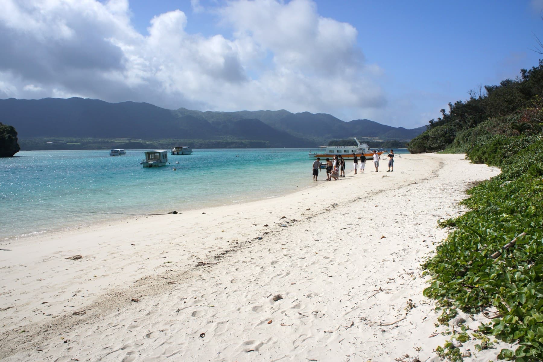 A curve of white sand runs along the edge of Kabira Bay as a few visitors walk down to the glass-bottom boats pulled up at the shore.