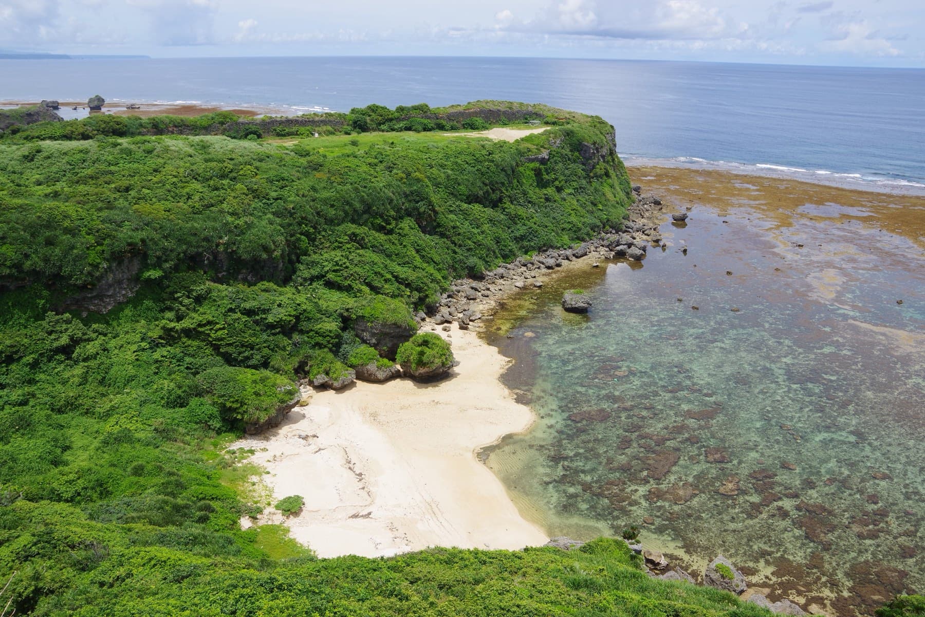 From the Kafu Banta lookout on Miyagi a small white sand cove sits below green cliffs, and a shallow reef flat runs out to the open Pacific