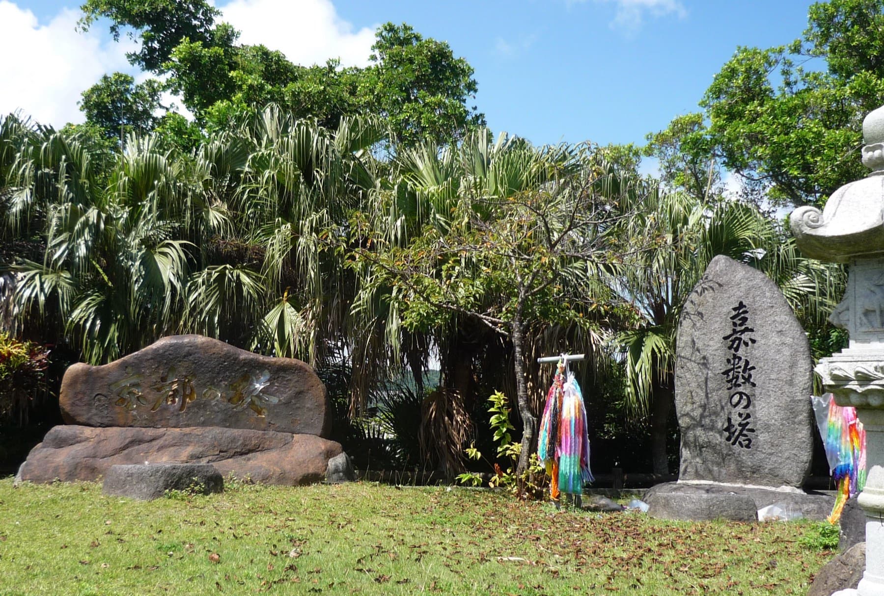 The Kakazu and Kyoto memorial stones stand among palms at Kakazu Takadai Park in Ginowan, with strings of folded paper cranes hung between them