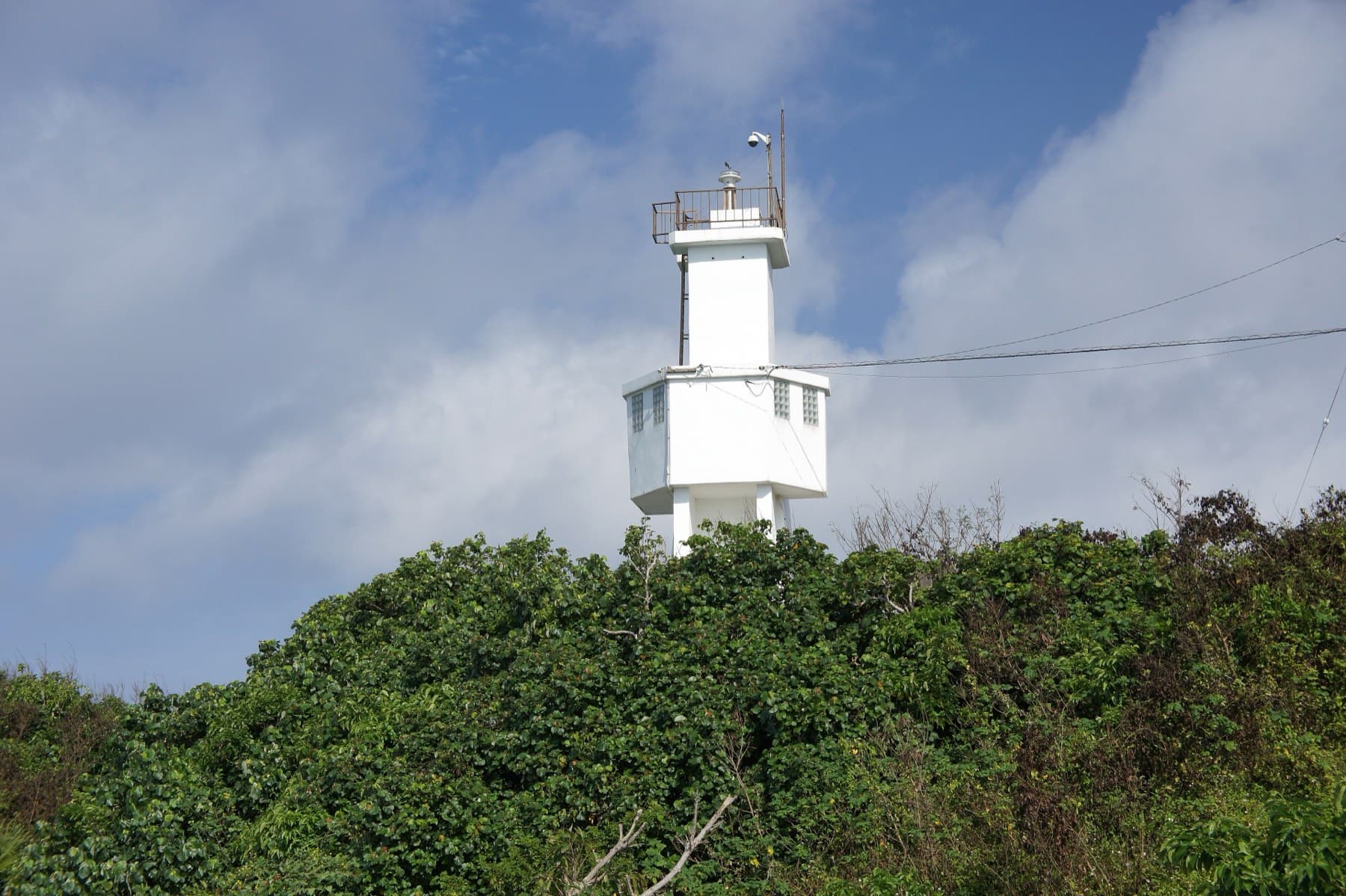 A concrete seawall walk leads along clear shallow water to the small white Kannonzaki lighthouse on its wooded point west of Ishigaki town.