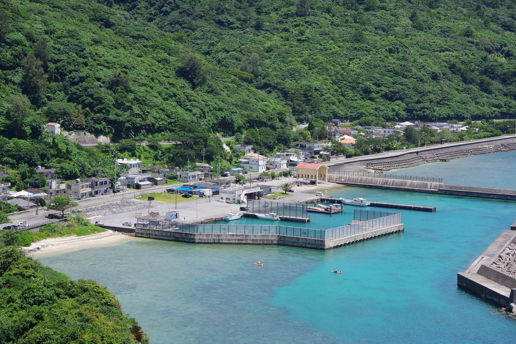 The small village and harbour of Ginama sit at the foot of steep forested hills, seen from the Kayauchi Banta lookout above clear blue water