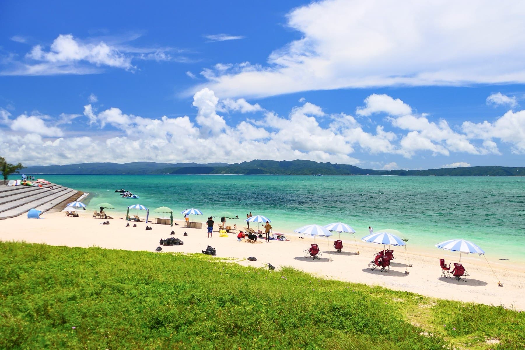 Parasols dot the white sand on the east side of Kouri Beach as the water turns from pale green to turquoise toward the hills of the main island