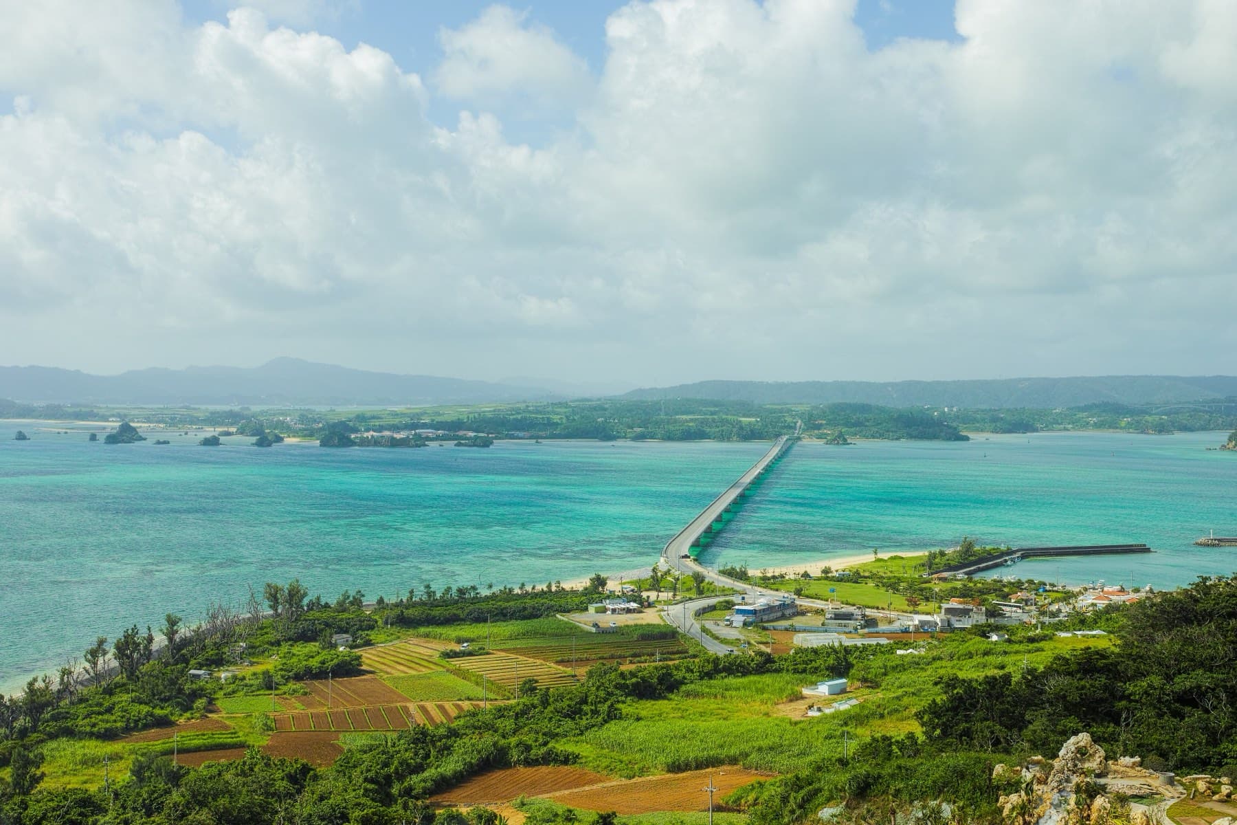 From the Kouri Ocean Tower the bridge runs in a thin line over turquoise shallows to Yagaji, with sugarcane fields and red earth in the foreground