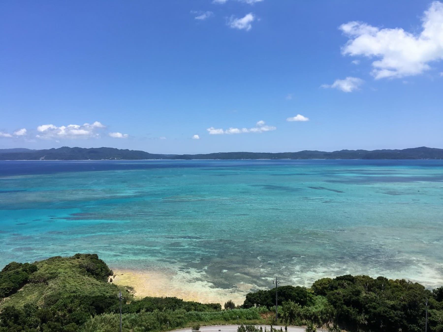 From the Kouri Ocean Tower the reef spreads in bands of turquoise and deep blue across the channel toward the long green coast of the main island