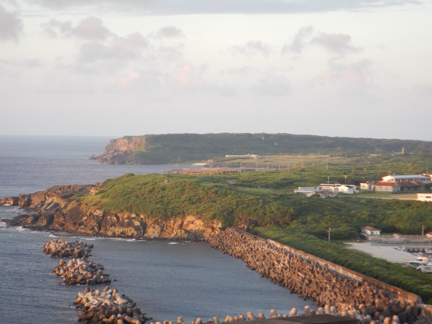 The low rocky point of Kubura-bari reaches into the sea past the breakwaters of Kubura harbour, seen from the Irizaki side.