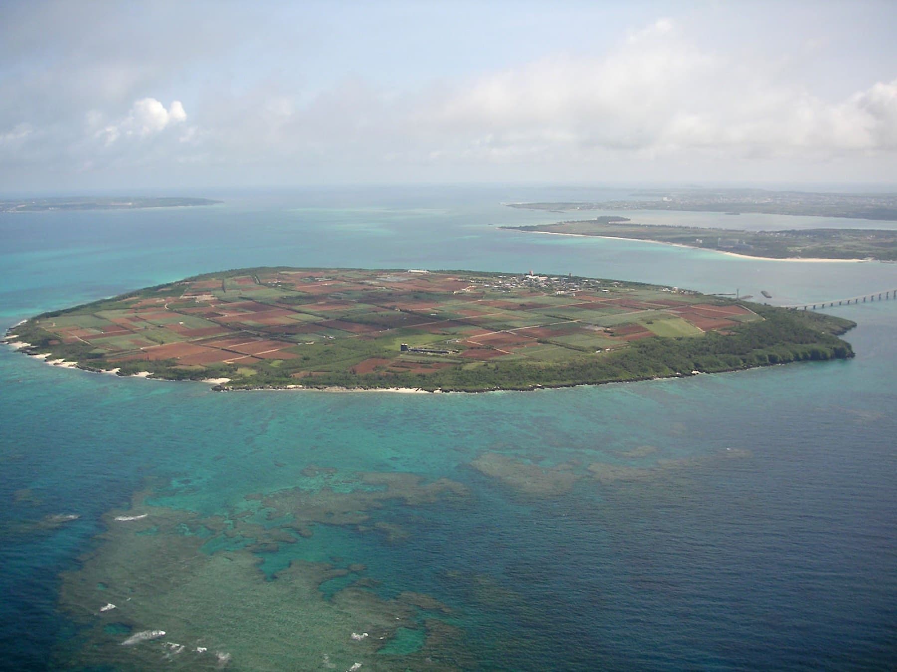 Kurima lies as a flat green disc of fields in a wide reef lagoon, and the Kurima Bridge reaches across to Miyako on the right.