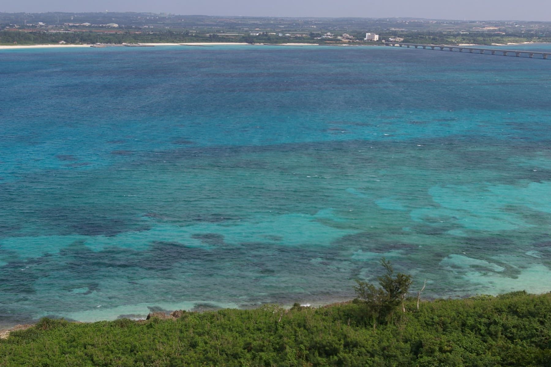 Patches of coral turn the shallow sea off Kurima into a pattern of turquoise and dark blue that runs toward the low coast of Miyako.