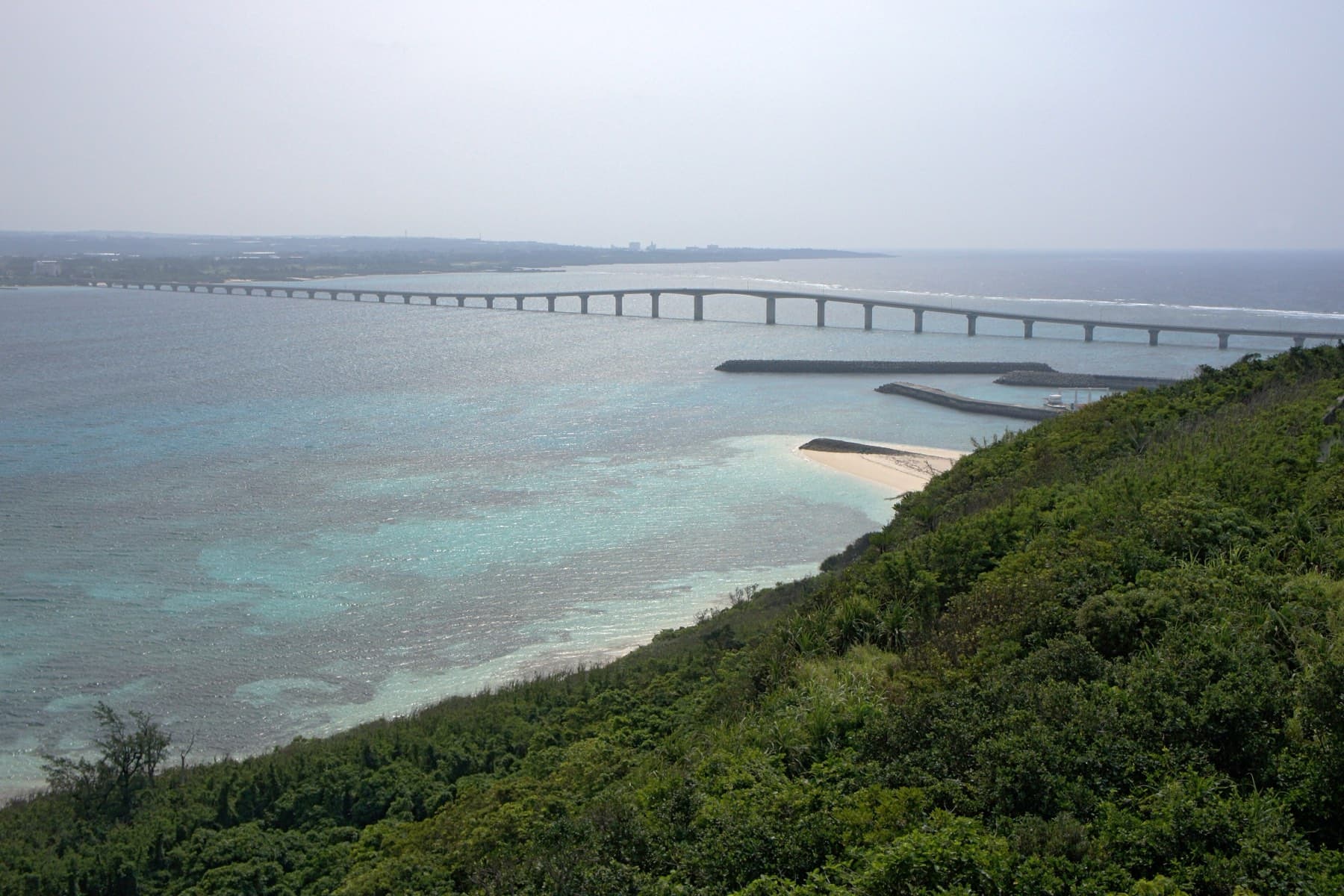 From the wooded hillside on Kurima the Kurima Bridge runs across shallow reef water toward Miyako and the sweep of Yonaha Maehama.