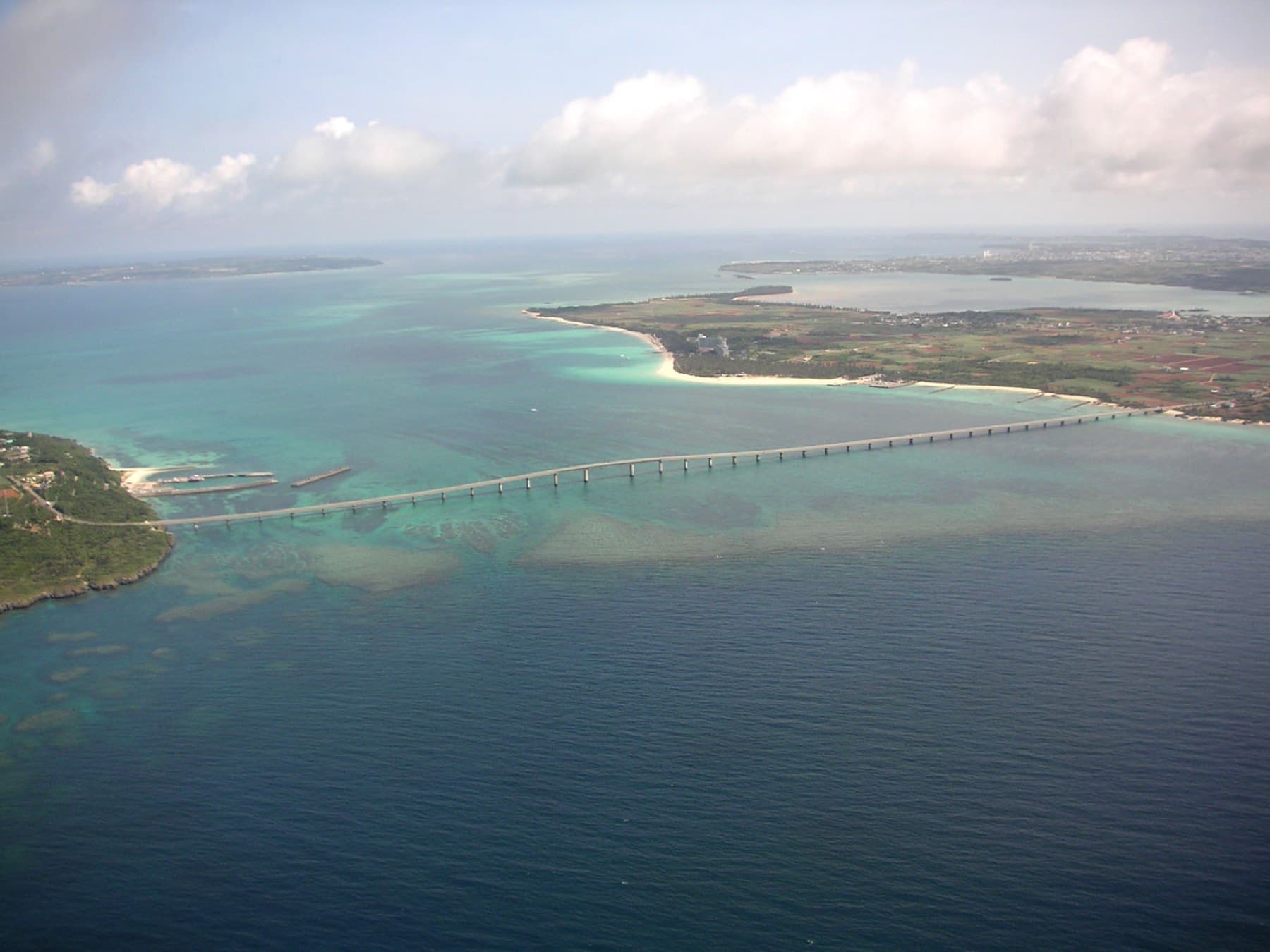 The Kurima Bridge links the green tip of Kurima to the flat farmland of southern Miyako across a pale reef in this view from high above.