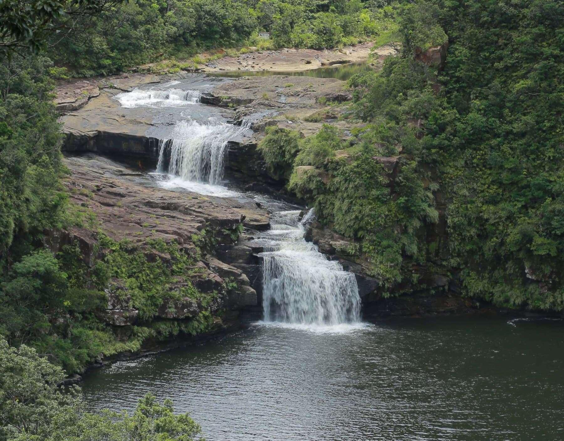 Two tiers of Mariyudu Falls tumble over grey rock ledges into the pool below under a canopy of jungle green.