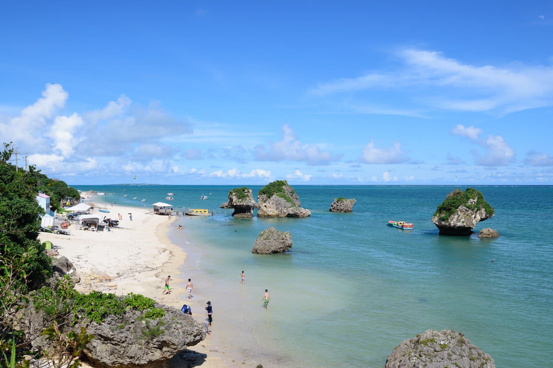 Mushroom-shaped rocks stand in calm green shallows off Mibaru Beach, where swimmers wade and glass-bottom boat shelters line the sand