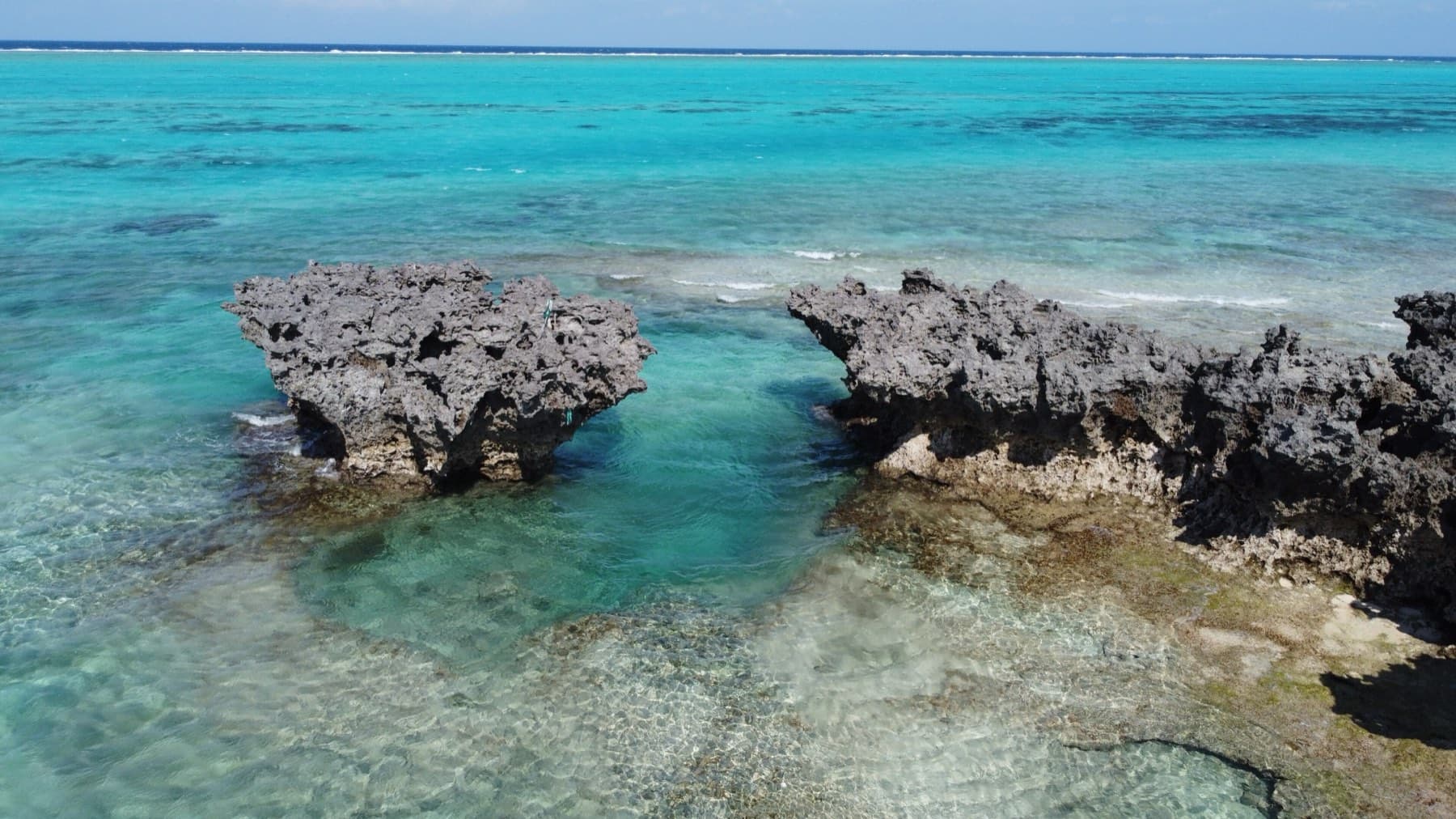 Two jagged coral rocks rise from turquoise water over the reef at Minata Beach in this drone view from above.